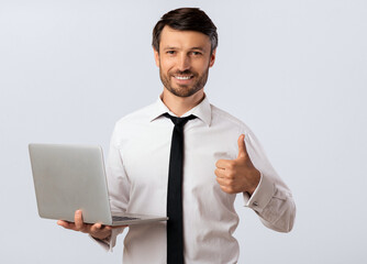 Like. Smiling Man Holding Laptop Gesturing Thumbs-Up Approving Computer Software. White Studio Background