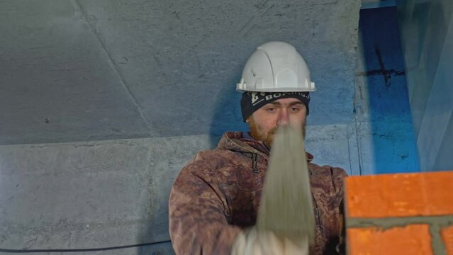 Man makes brickwork at construction site. Clip. Uniformed worker makes brickwork inside house. Man makes brick wall in house