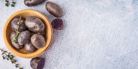 Wooden bowl of raw purple potatoes and thyme on light grunge background with space for text
