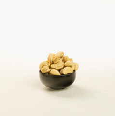 cashew nuts in a woven bamboo container and a black bowl on a plain white background