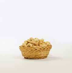 cashew nuts in a woven bamboo container and a black bowl on a plain white background