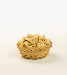 cashew nuts in a woven bamboo container and a black bowl on a plain white background