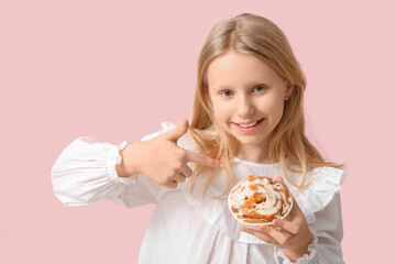 Cute little girl pointing at tasty cinnamon bun on color background