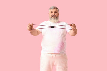 Overweight happy mature man with fitness expander on pink background. Weight loss concept