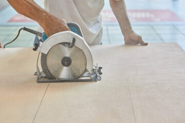Midsection of man using circular saw cutting wooden board 
