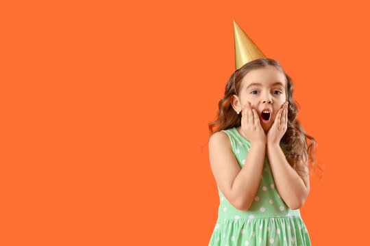 Shocked little girl in party cone on orange background - Powered by Adobe
