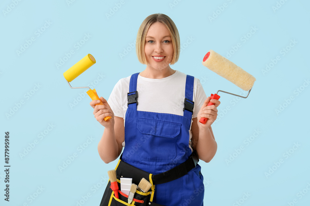 Wall mural female decorator with paint rollers on blue background