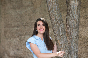 young and beautiful latin woman, clinging to a tree smiles and looks at different places, the woman looks around and is happy in the city she is on holiday.