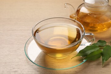 Refreshing green tea in cup, leaves and teapot on wooden table, closeup