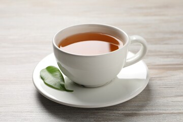 Refreshing green tea in cup and leaf on grey wooden table, closeup