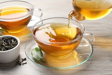 Pouring refreshing green tea into cup at grey wooden table, closeup