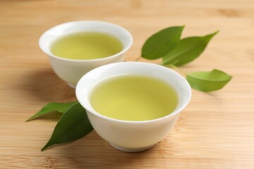 Refreshing green tea in cups and leaves on wooden table, closeup
