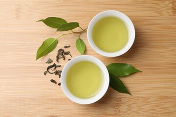 Refreshing green tea in cups and leaves on wooden table, flat lay