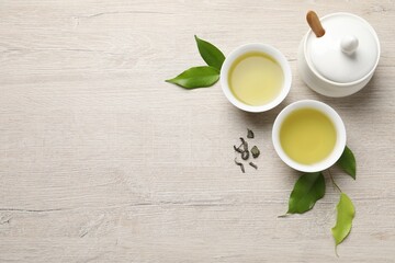 Refreshing green tea in cups, sugar bowl and leaves on wooden table, flat lay. Space for text