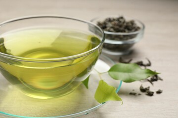 Refreshing green tea in cup and leaves on wooden table, closeup