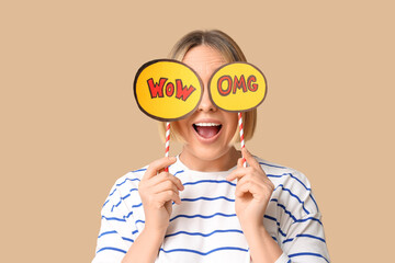 Surprised adult woman holding speech bubbles with words OMG and WOW on beige background