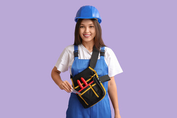 Young female worker with tool belt on lilac background
