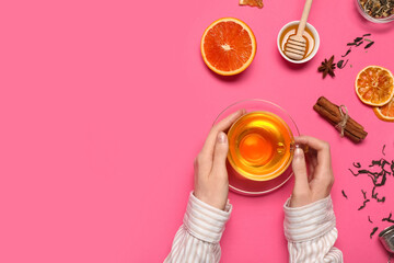 Female hands holding cup of tea, orange and cinnamon sticks on pink background