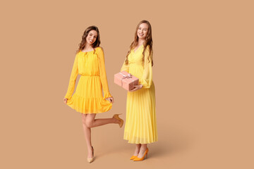 Beautiful young sisters with gift box on beige background