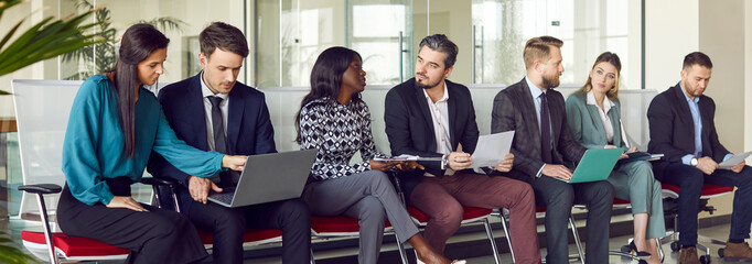 Young diverse business people sitting on chairs in a row with resumes and laptops in hands chatting and talking with each other. Job candidates seekers waiting for interview invitation turn. Banner