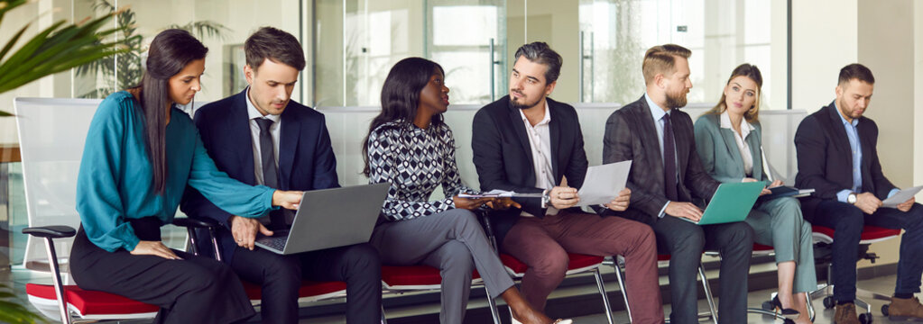 Young diverse business people sitting on chairs in a row with resumes and laptops in hands chatting and talking with each other. Job candidates seekers waiting for interview invitation turn. Banner