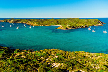Aerial view of Es Grau beach in Menorca during a sunny summer day. Pristine beach with blue clean waters, drone landscape of balearic island of Menorca