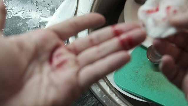 Close-up of a hand with cut finger being treated with a cotton pad to stop the bleeding while washing dishes, highlighting first aid care in everyday kitchen accidents
