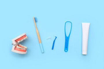 Jaw model with toothbrush, toothpaste and tongue scraper on blue background