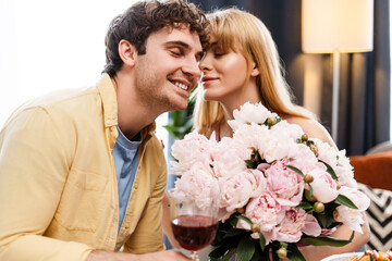 Young man giving bouquet of peonies to woman holding glass of wine