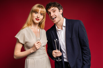 Elegant couple smiling and holding champagne glasses isolated on red background