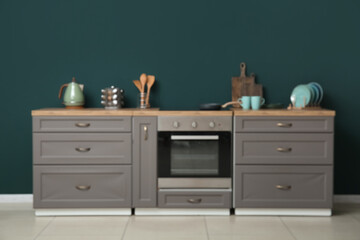 Blurred view of modern kitchen with grey counters, stove and utensils near green wall