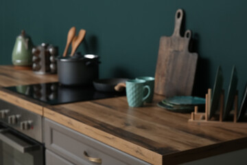 Blurred view of modern kitchen with grey counters, stove and utensils near green wall