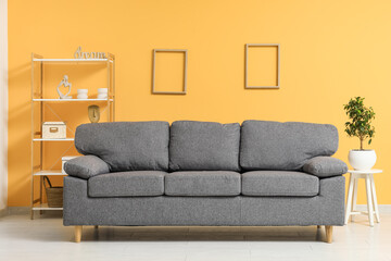 Stylish living room with black sofa, coffee table and shelving unit near orange wall