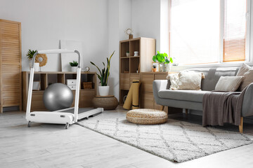 Interior of cozy living room with treadmill, shelf units and sofa