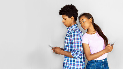 African American teen couple standing back-to-back against a gray wall. They are both looking down...
