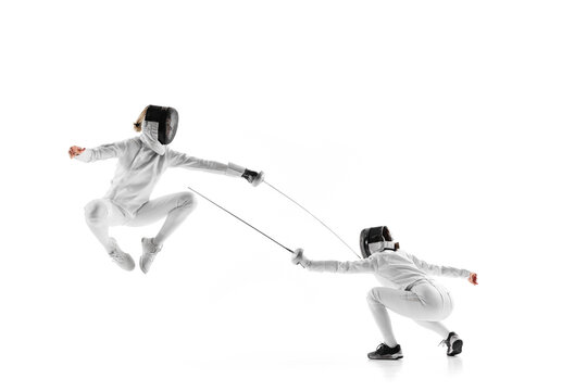 Two young girls, athletes during intense fencing duel, showcasing their skill and agility against white studio background. Concept of professional sport, competition, strength and power, action. Ad