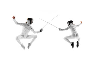 Practicing their fencing skills, two young girls, athletes demonstrate their agility and precision in spirited duel against white studio background. Concept of professional sport, competition, action.