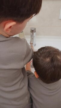 boy and baby child in bathroom,brushing teeth,washing hands with soap,combing hair.siblings,brothers in front of sink on tabouret chair.kids on toilet with lot of paper.