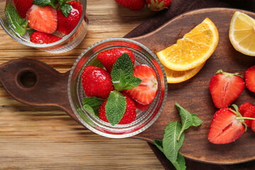 Glass of infused water with strawberries and mint on wooden background