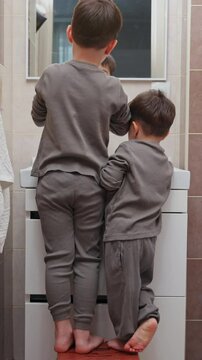 boy and baby child in bathroom,brushing teeth,washing hands with soap,combing hair.siblings,brothers in front of sink on tabouret chair.kids on toilet with lot of paper.