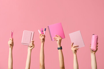 Many hands with notebooks, stationery and pencil case on pink background