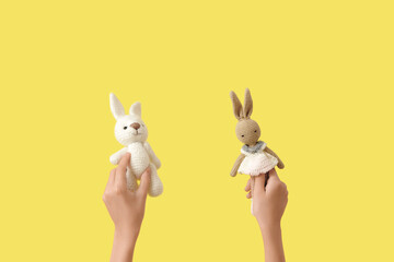 Child with knitted toy bunnies on yellow background