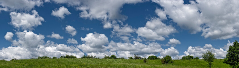 Panoramaaufnahme von Schönwetterwolken und Haufenwolken über einer grünen Wiese
