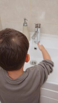 boy and baby child in bathroom,brushing teeth,washing hands with soap,combing hair.siblings,brothers in front of sink on tabouret chair.kids on toilet with lot of paper.