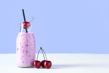 Bottle of fresh smoothie with cherries on blue background