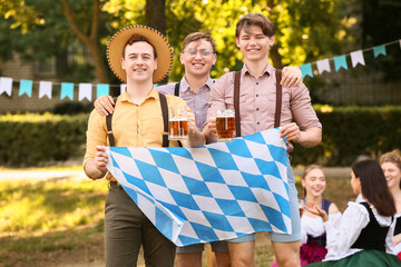 Young men in traditional clothes with Bavarian flag celebrating Octoberfest outdoors