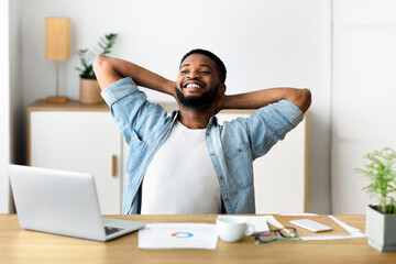 Smiling millennial businessman having rest at contemporary working place, leaning back in chair