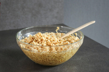 Close up of soy bean meat mince sucked up in water in a glass bowl with a wooden spoon, grey...