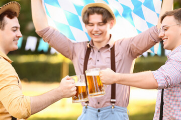 Young men in traditional German clothes with beer and Bavarian flag celebrating Octoberfest outdoors, closeup