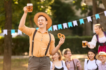 Fototapeta premium Young man in traditional German clothes with beer and pretzel celebrating Octoberfest outdoors
